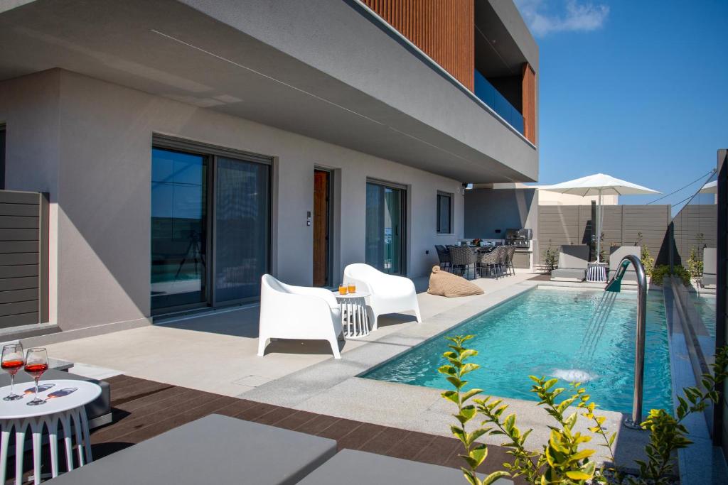 a patio with a swimming pool and white chairs at Villa Nectar in Kounoupidhianá