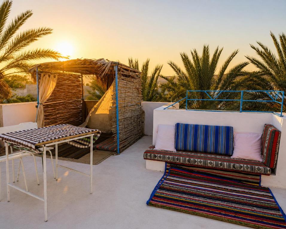 a patio with a bench and a table and palm trees at Dar Essadeg in Tataouine