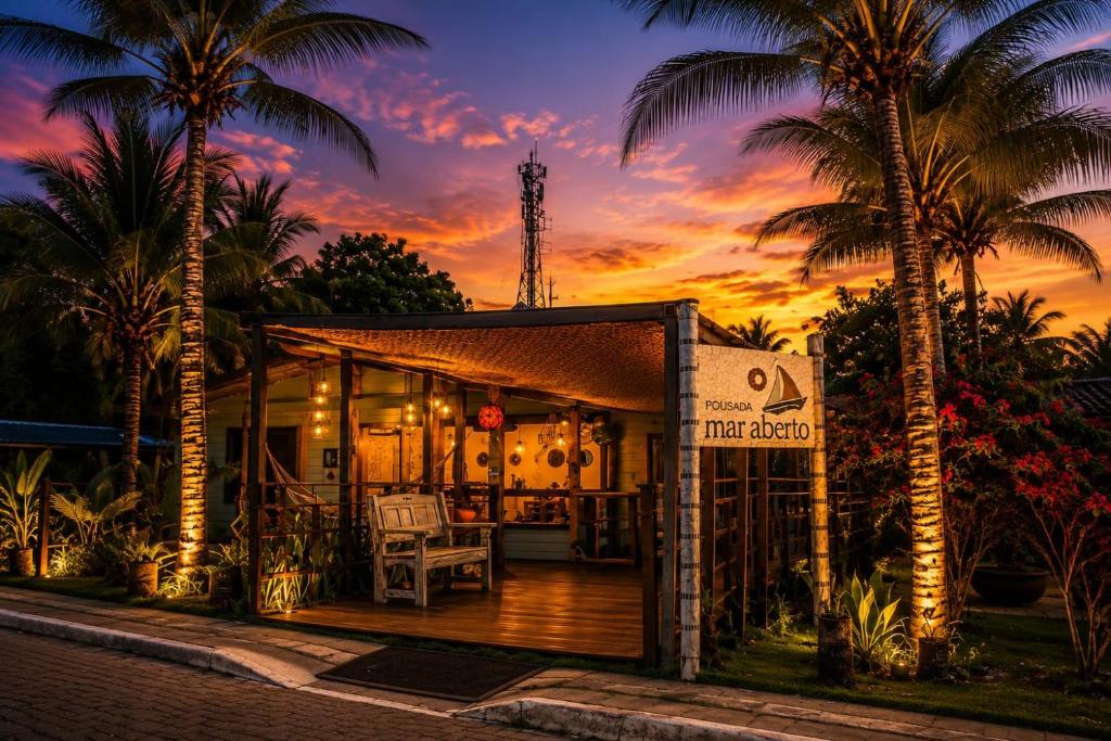 a restaurant with a deck with palm trees and a sunset at Pousada Mar Aberto in Fernando de Noronha