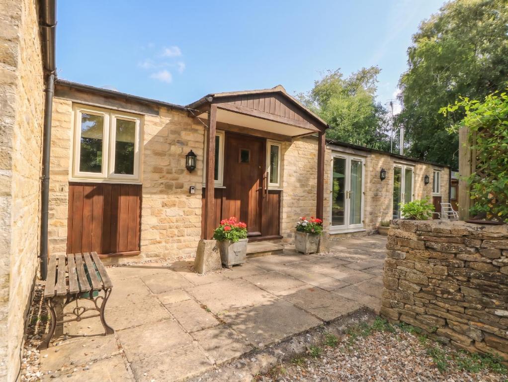a stone house with a bench in front of it at Meadow Lodge in Cirencester