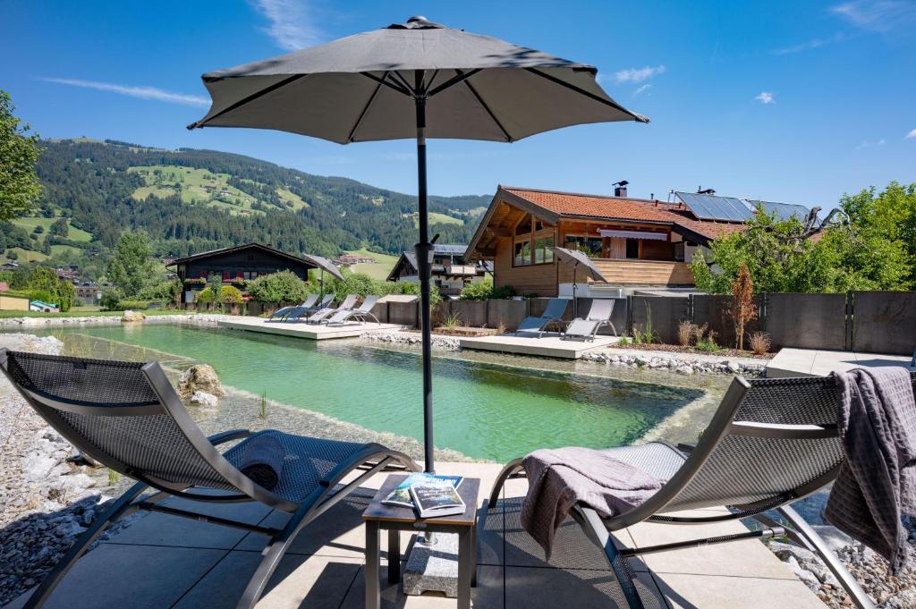 a patio with two chairs and an umbrella next to a pool at Appartements Andrea Cäciel - Alpline Appartements KG in Brixen im Thale