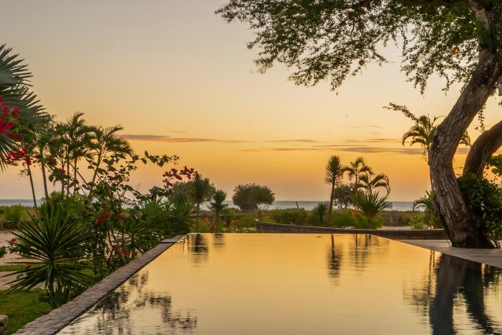 a pool in a resort with a sunset in the background at Villa Praia - La Villa Group in Jericoacoara