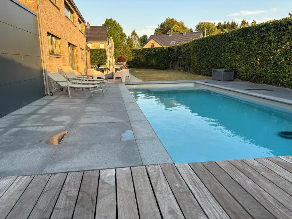 a swimming pool with a wooden deck next to a house at Maison des W in Jalhay