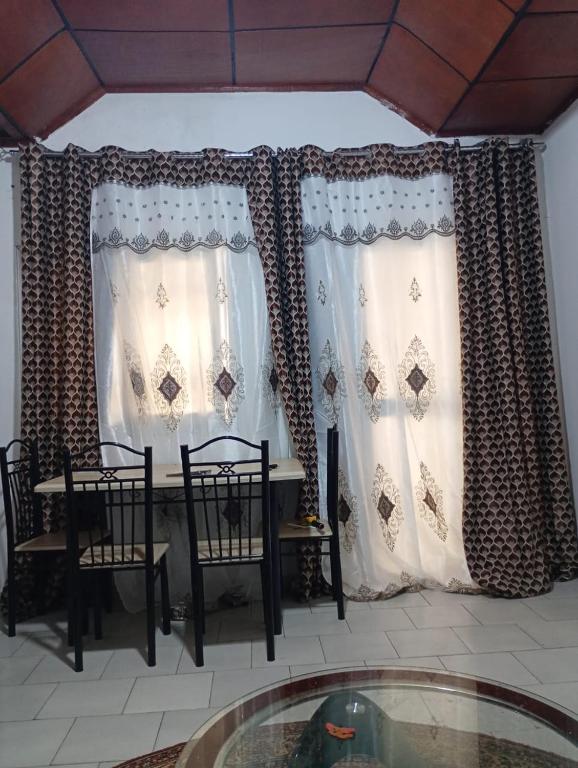 a dining room with a table and chairs and curtains at Cosy appartement à Nongo in Conakry