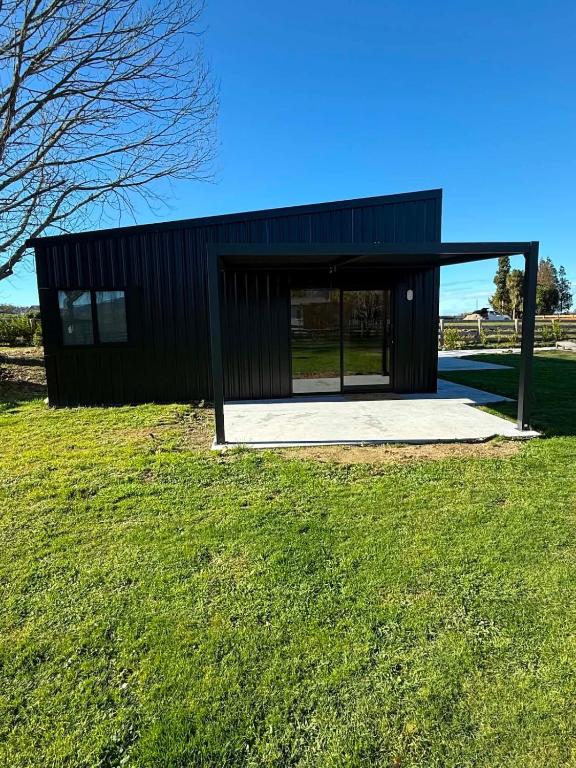 a black house on a grassy field with a building at Pirongia Views Studio in Pirongia