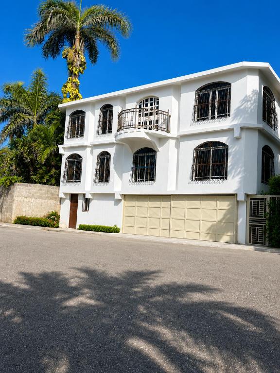 a white house with a palm tree in front of it at Los Patos Waterfront Private Suites in Los Patos
