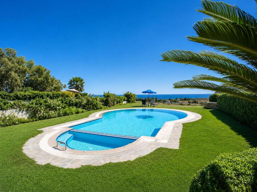 an image of a swimming pool in a lawn with a palm tree at Villa Seashell in Pefki