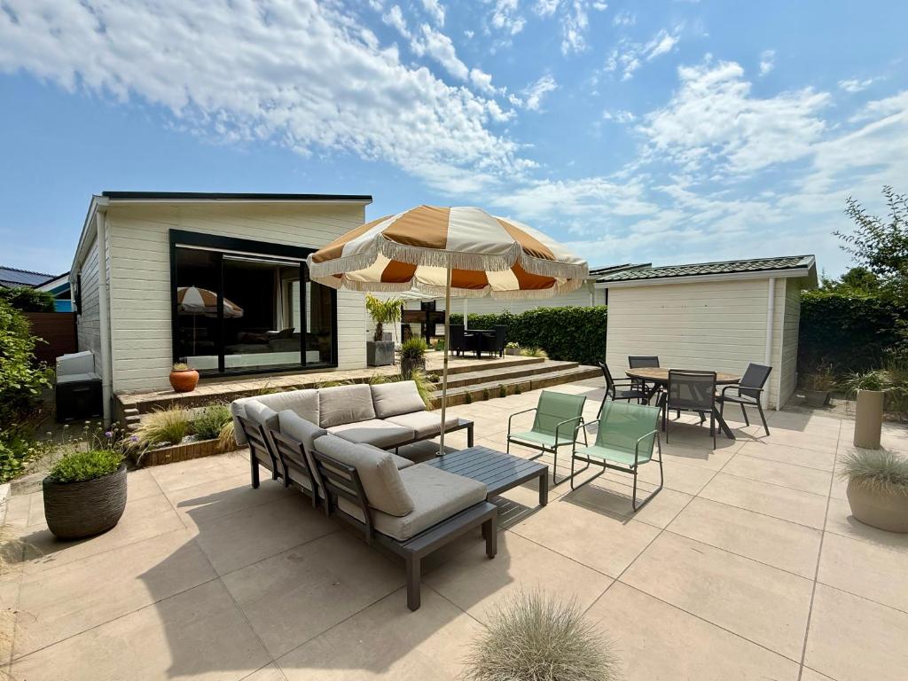a patio with an umbrella and chairs and tables at Vakantiewoning De Bosrand Aan Zee in Sint Annaland
