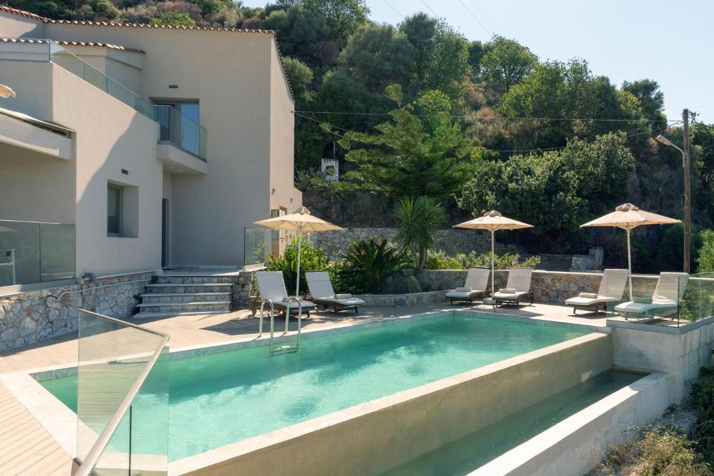 a pool with chairs and umbrellas next to a house at Villa Dorothea in Georgioupoli