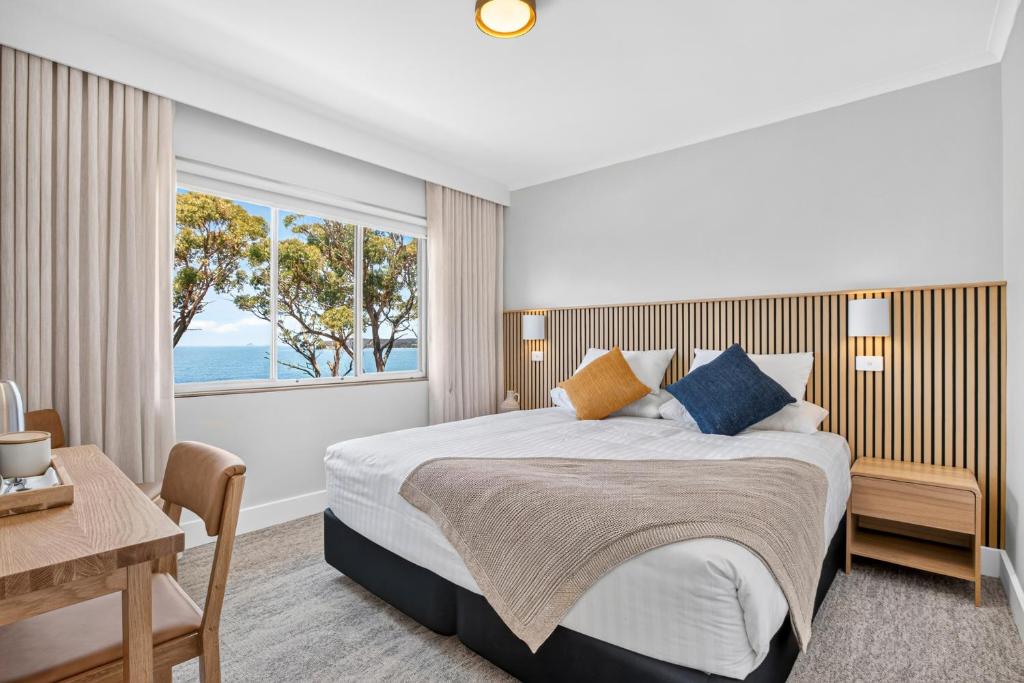 a bedroom with a bed and a desk and a window at Lufra Beachside Hotel in Eaglehawk Neck