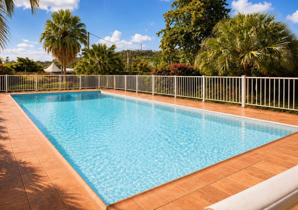 a large swimming pool with a fence and palm trees at Le Palmier Bleu, Spacious Duplex with Pool in Schœlcher