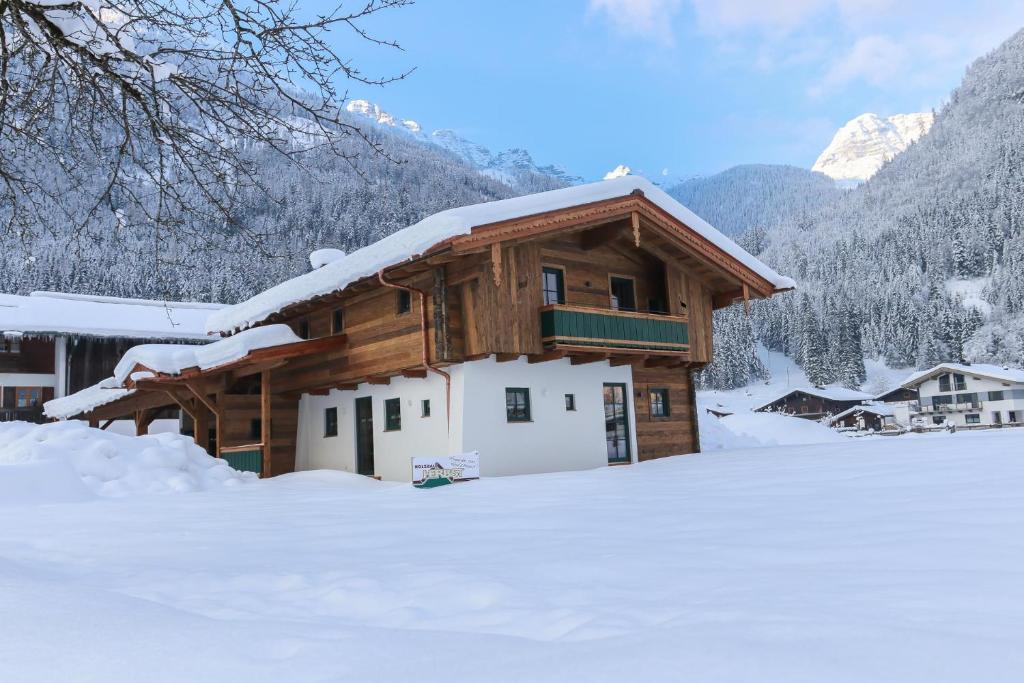uma cabana de madeira coberta de neve com montanhas ao fundo em Chalet am Müllergut em Sankt Martin bei Lofer
