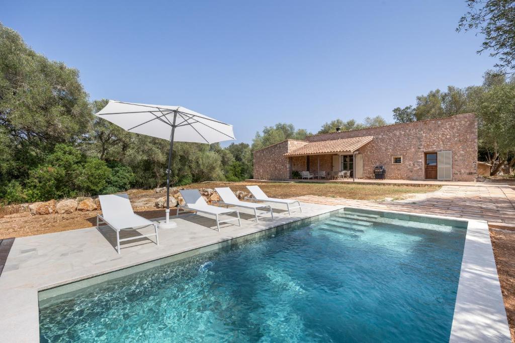 a pool with chairs and an umbrella next to a house at Villa Biniali Costitx in Costitx