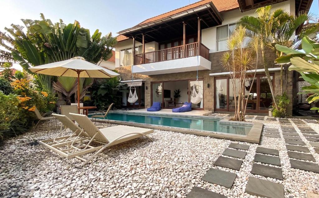 a house with a pool and two chairs and an umbrella at Villa Dew Canggu in Kerobokan
