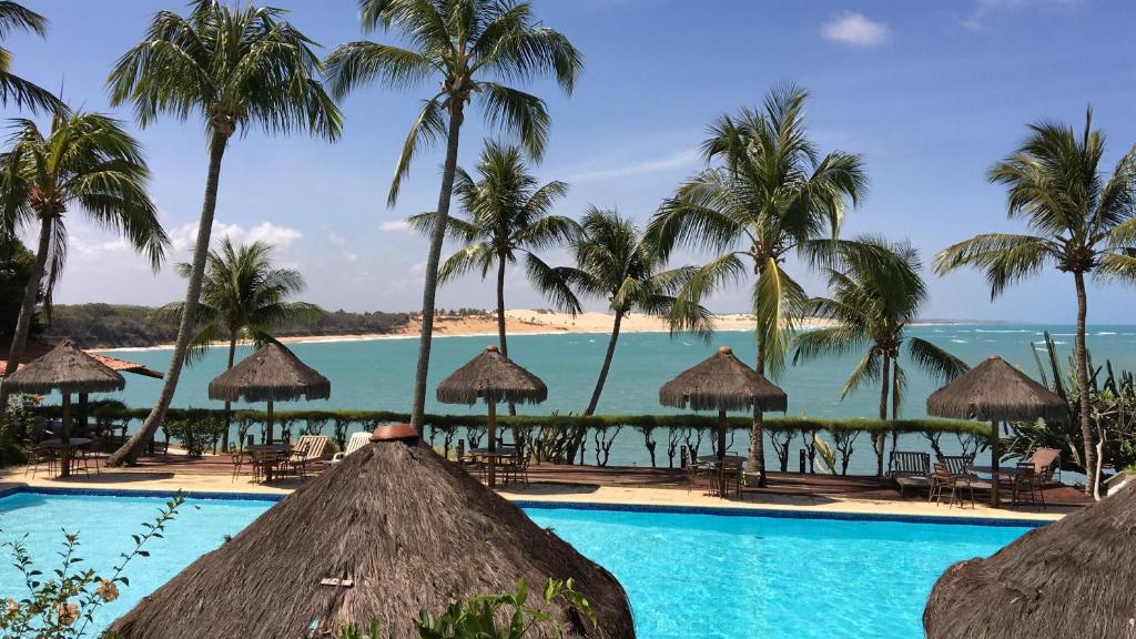 uma piscina com palmeiras e o oceano ao fundo em Hotel Marinas em Pipa