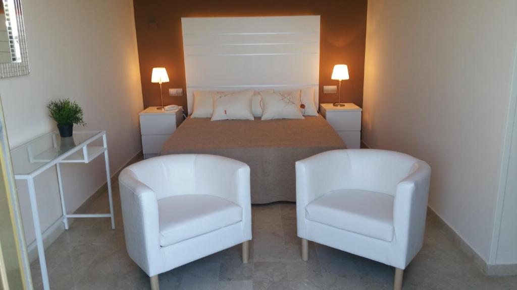 a bedroom with a bed and two white chairs at Hotel L'Alguer in L'Ametlla de Mar