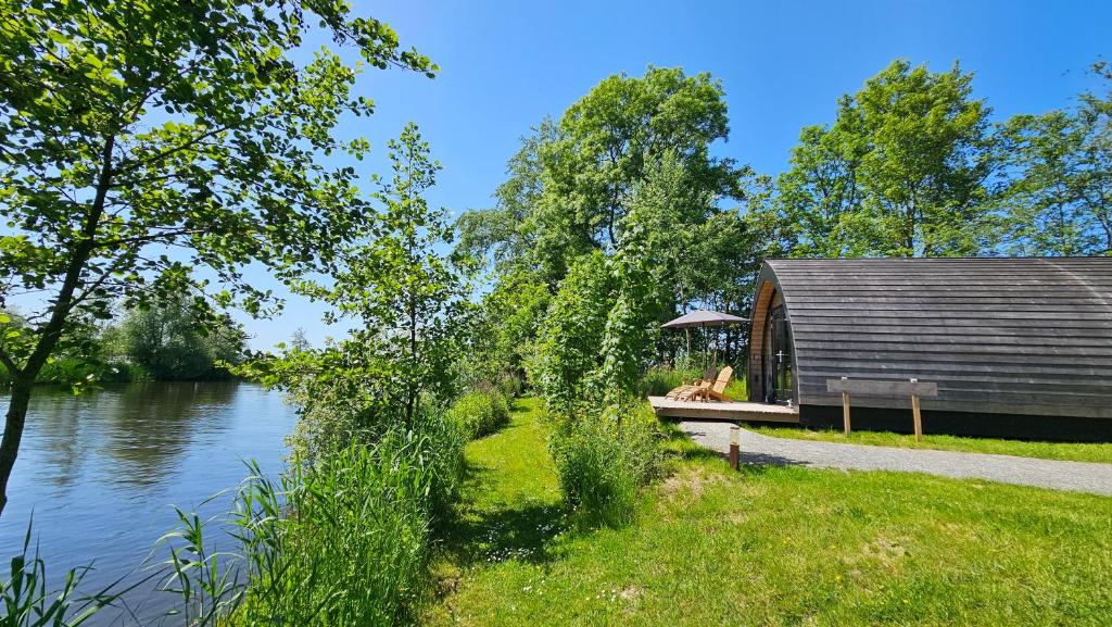a cabin by a river with a dog sitting on a bench at Tiny House De Houtekster in Westergeest