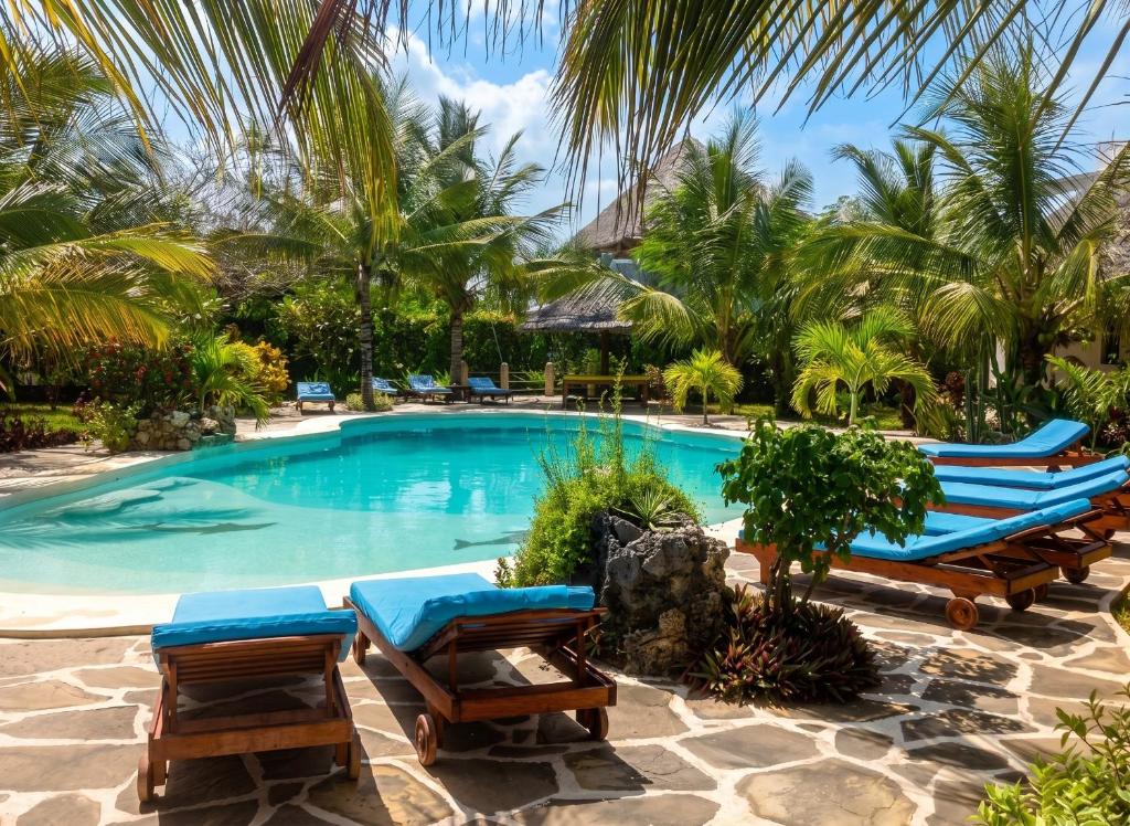 a swimming pool with lounge chairs and palm trees at Spacious accessible house in Watamu, shared pool in Watamu