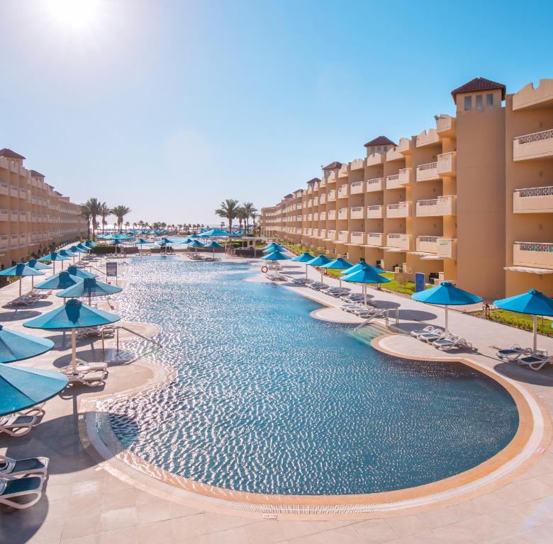 a swimming pool with blue umbrellas and chairs at Amwaj Beach Club Abu Soma in Hurghada