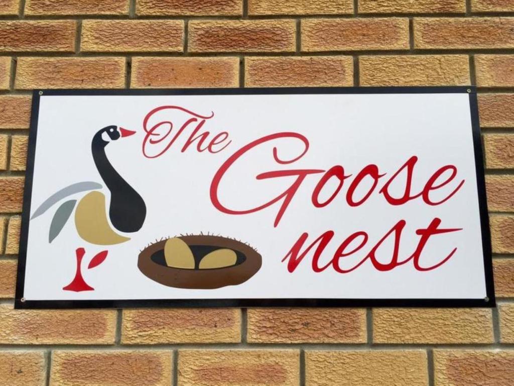 a sign on a brick wall with a goose and a nest at The Goose Nest in Struisbaai