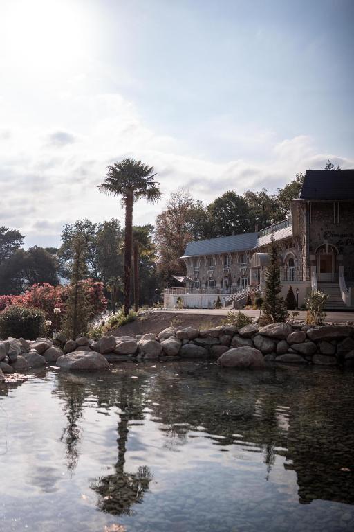 a building with a palm tree next to a pond at Domaine de Beaucens in Beaucens