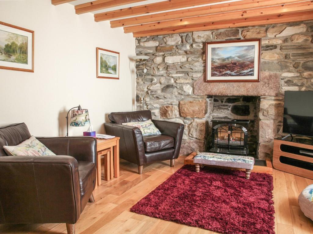 a living room with two chairs and a stone fireplace at Hill Cottage in Ardmair