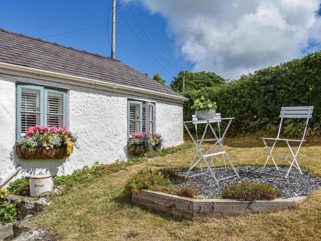 a small white house with two chairs and flowers at Tan Bryn - Uk44151 in Llanallgo