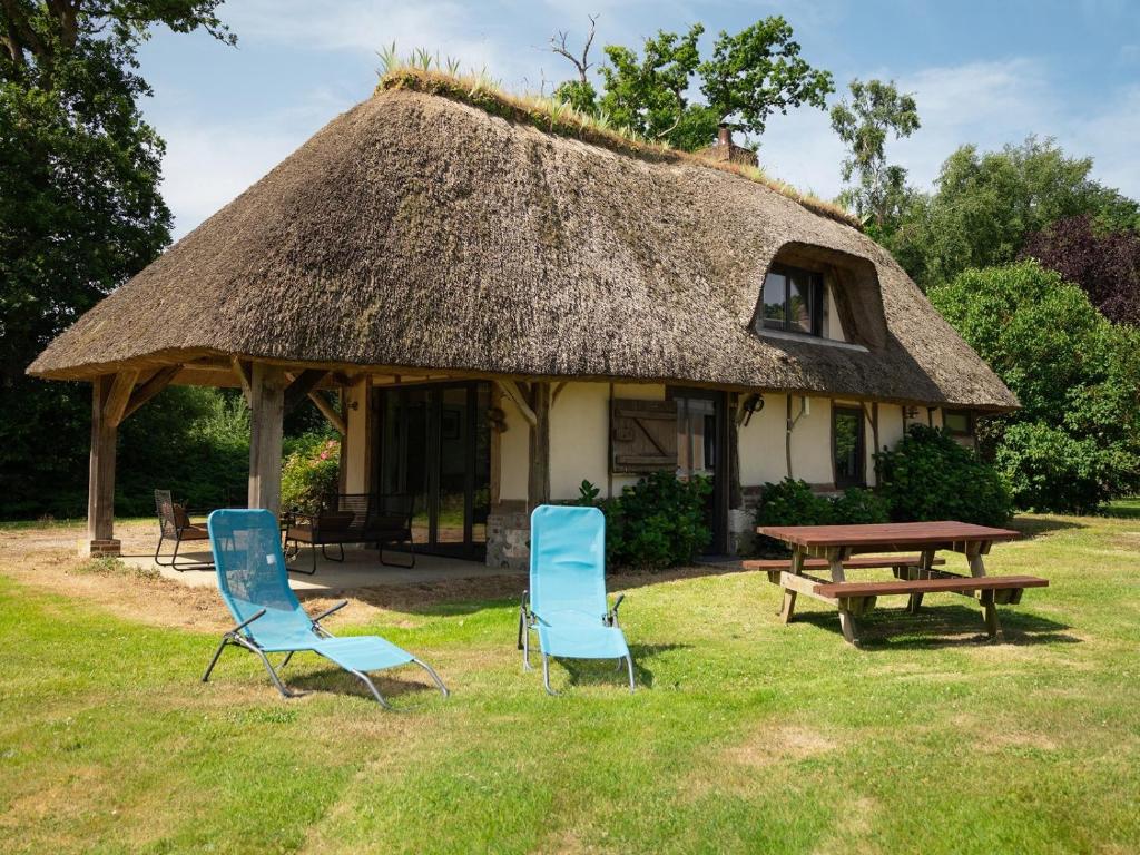 a house with two chairs and a table and a thatch roof at La Chaumière in Flancourt-Catelon