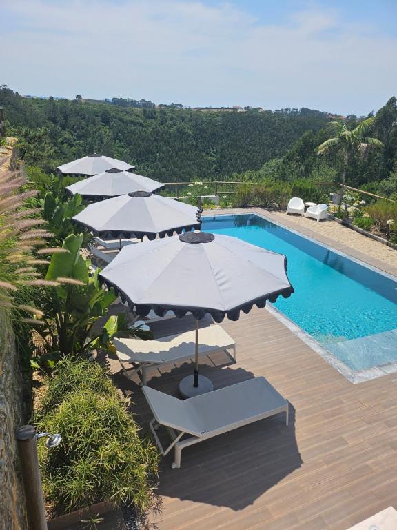 a group of umbrellas and chairs next to a swimming pool at Quinta da Relva - Soulful House in Mafra