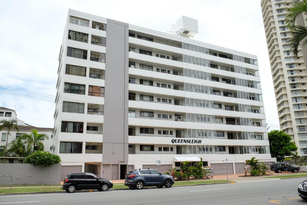 um grande edifício de apartamentos branco com carros estacionados em frente em Queensleigh Holiday Apartments em Gold Coast