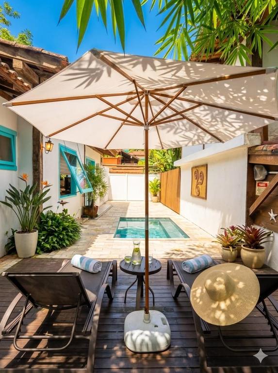 a patio with an umbrella and chairs and a pool at Zeisa House in Maresias