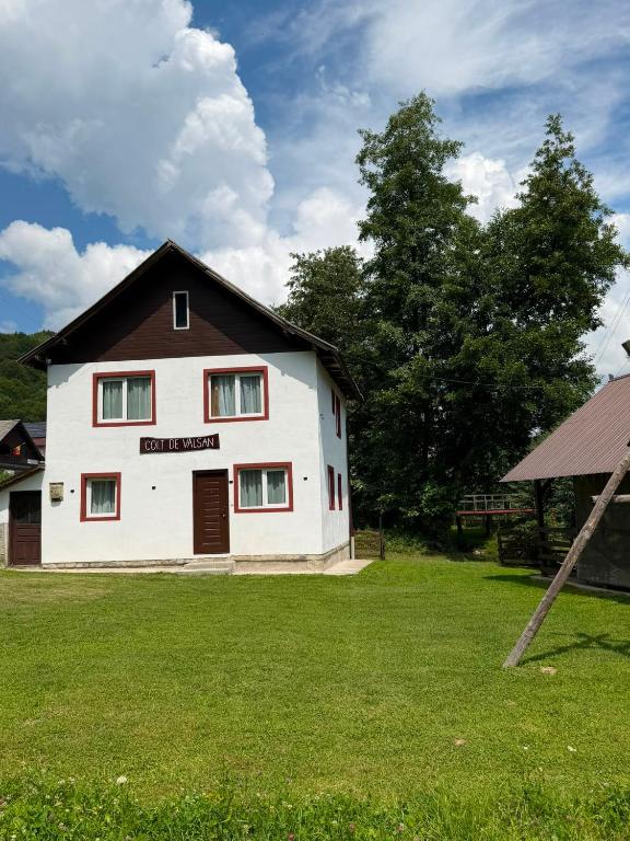 a white house with a black roof on a grass field at Colț de Vâlsan in Brăduleţ