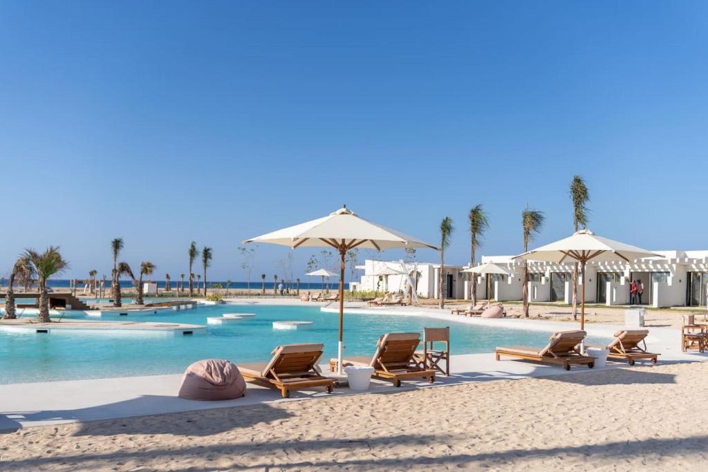a swimming pool with chairs and umbrellas on a beach at The Waterfront Cabins at D-Bay - Lemon Spaces in Zāwiyat ‘Abd al Mun‘im