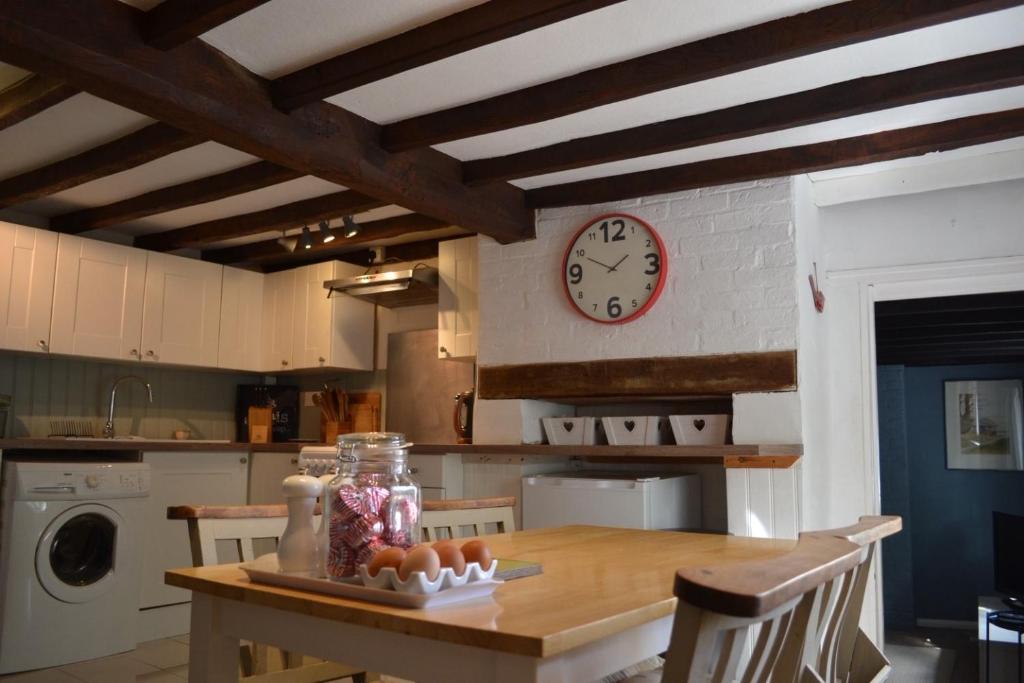 a kitchen with a wooden table with a clock on the wall at The Cottage in Sulgrave