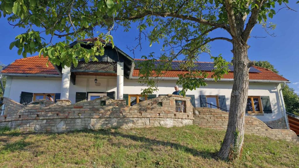 a house with a stone wall and a tree at Jakabhegy vendégház in Szenna