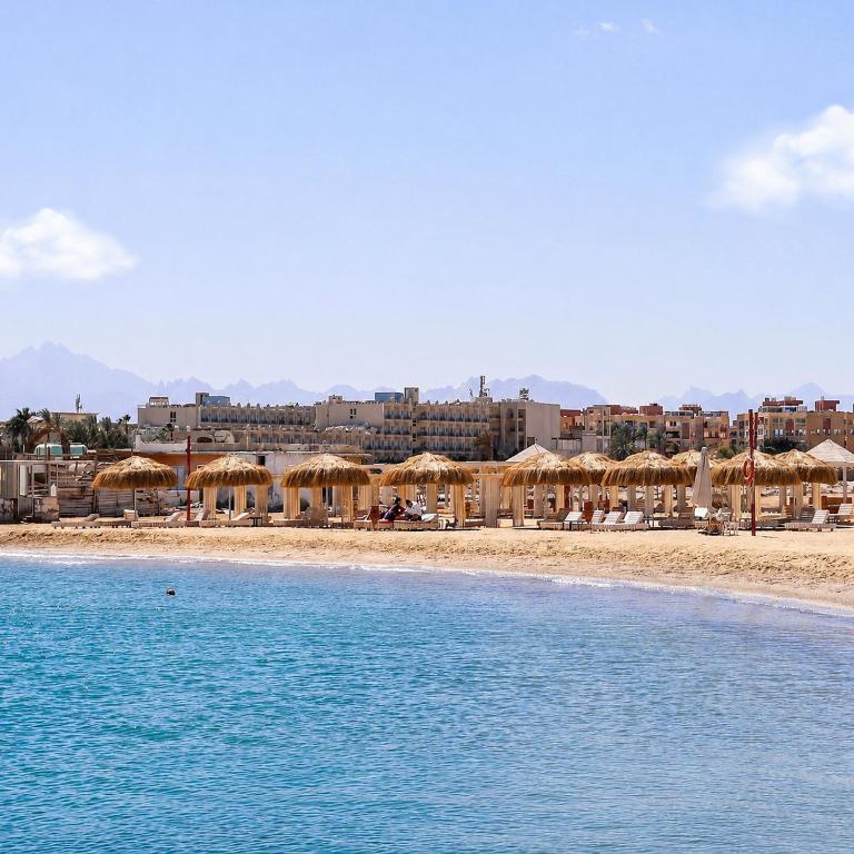 a beach with umbrellas and chairs and buildings at Alhambra First Avenue in Hurghada