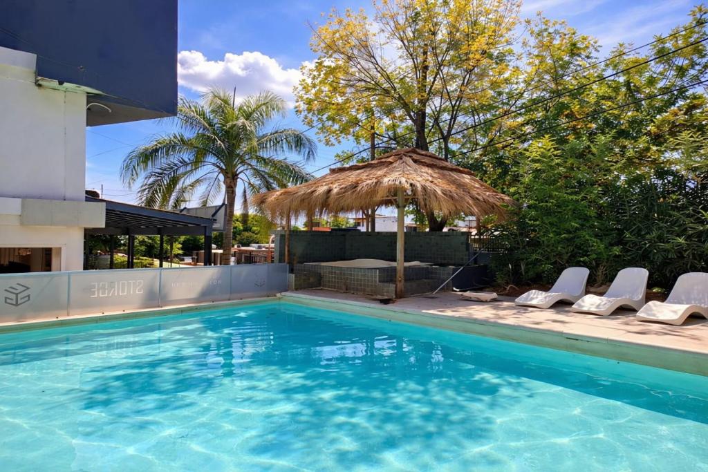 a swimming pool with chairs and a straw umbrella at Hotel Storge in Villa Carlos Paz