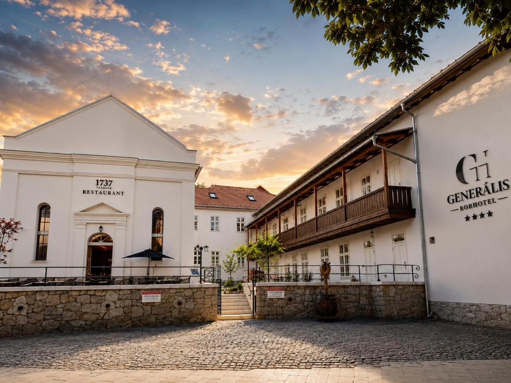 a large white building with a sunset in the background at Generalis Wine Hotel in Tokaj
