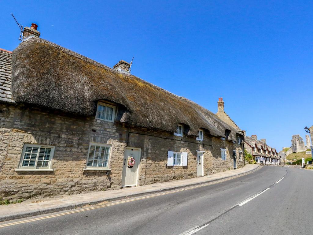 an old stone building with a thatched roof on a street at Little Wickers in Wareham