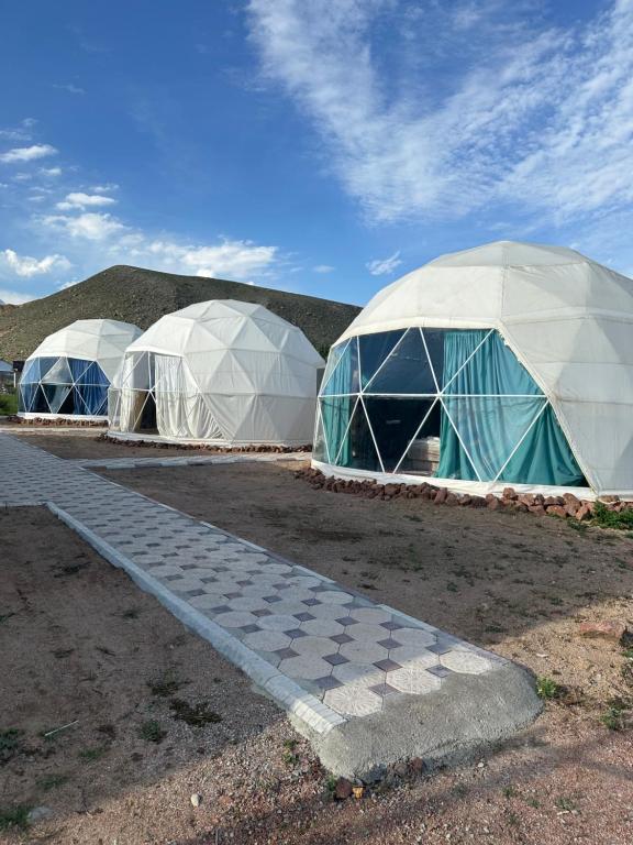 three domes are lined up in a field at Meykin Glamp in Cholpon-Ata