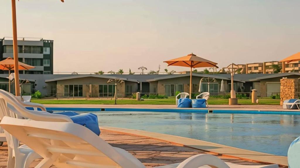 a swimming pool with white chairs and umbrellas at Marina Blu Blumar Chalet in Ain Sokhna