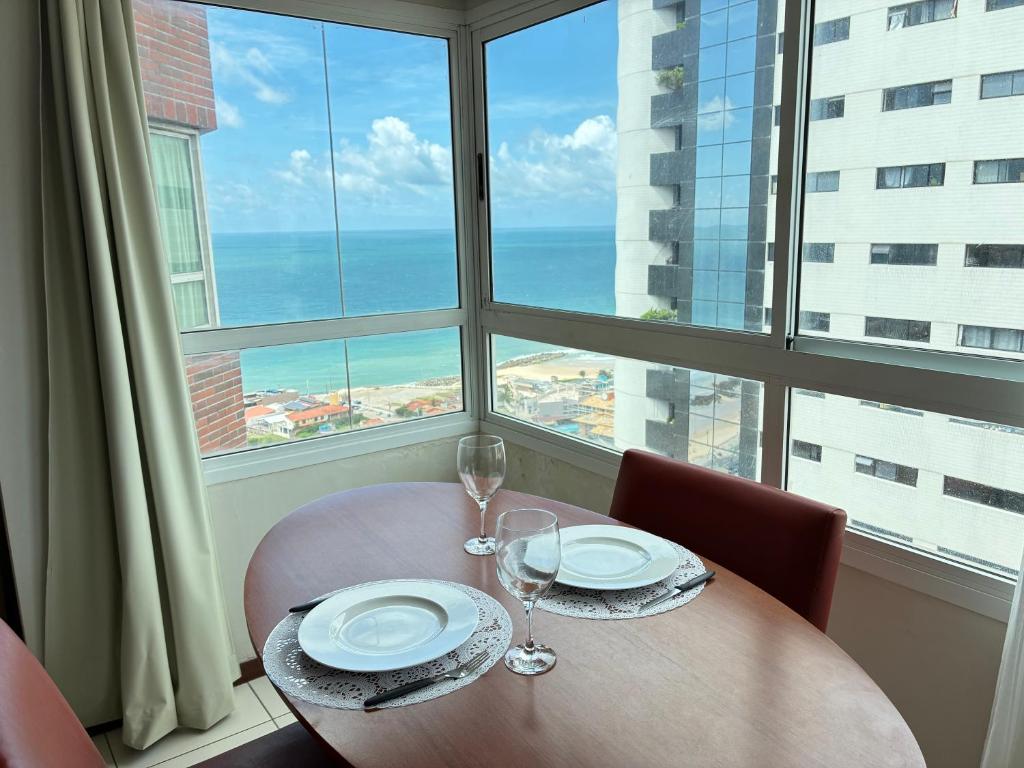a table with two plates and wine glasses in front of a window at Flat com vista para o mar - apto 1605 in Natal