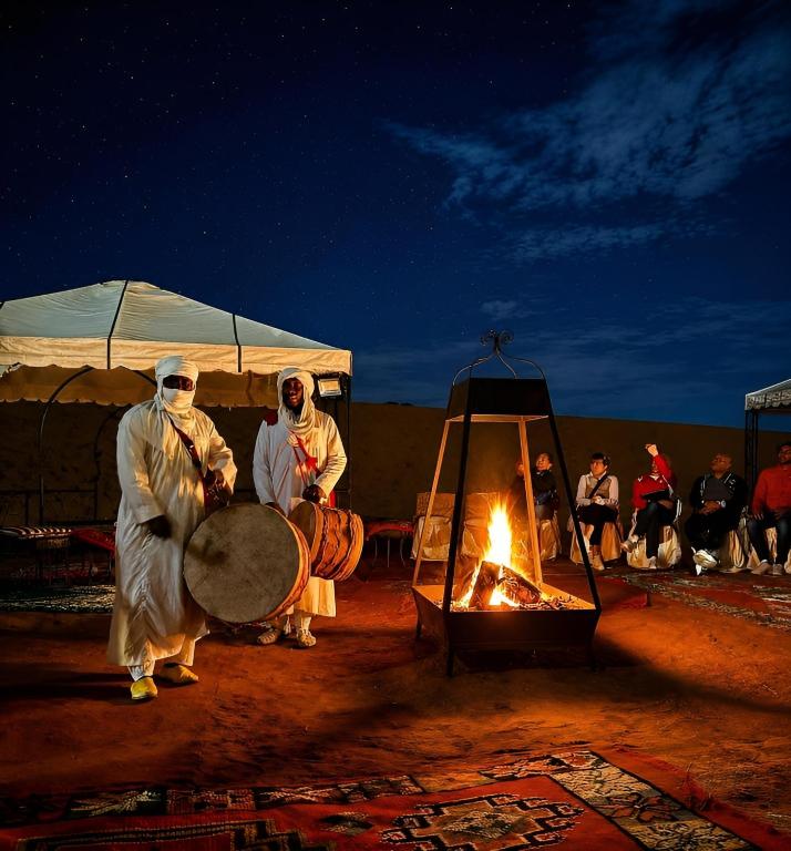 a group of people standing around a fire at Sahara Nights Luxury Camp in Merzouga