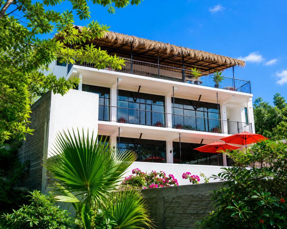 a white building with a red umbrella in front of it at Casa Esperanza in Playa Estacahuite