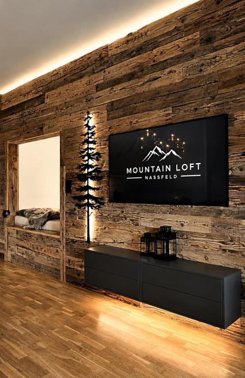 a room with a tv on a wooden wall at Mountain Loft Nassfeld in Tröpolach