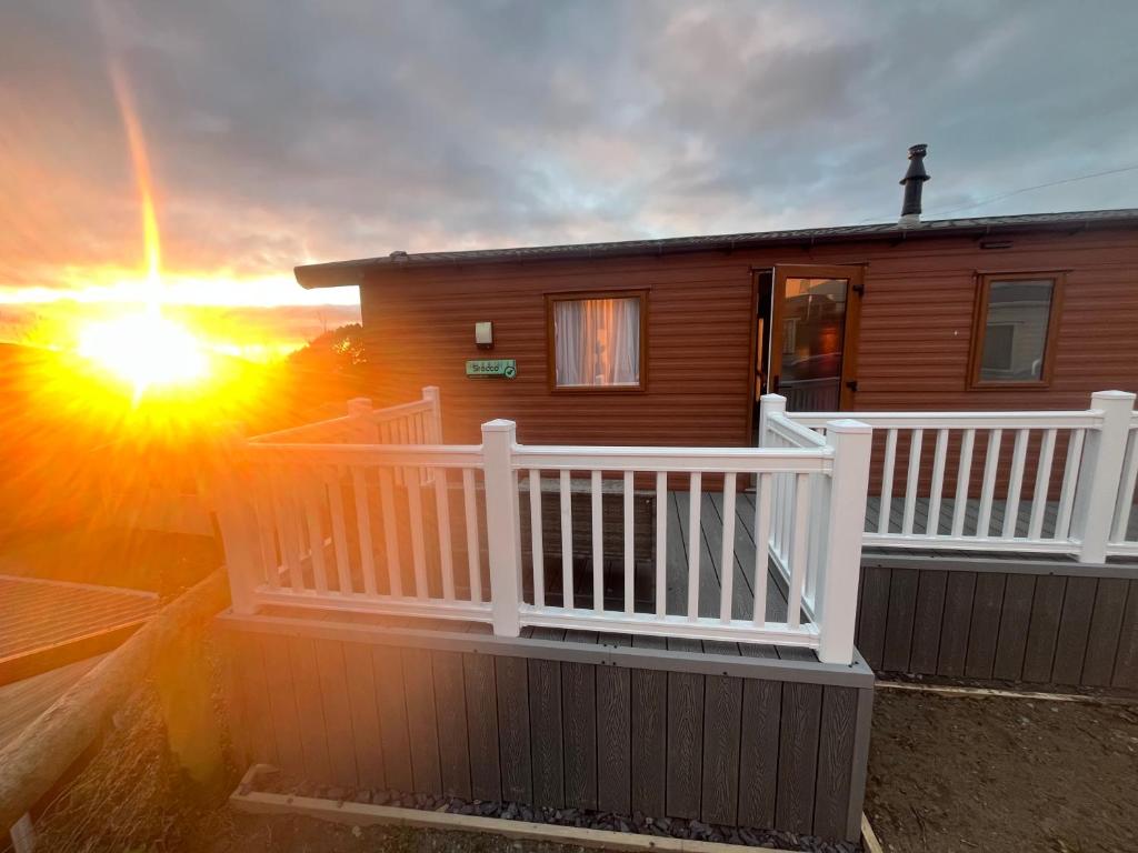 a house with a balcony with the sun setting behind it at Beautiful 3 Bed Caravan with Views & Decking in Mortehoe