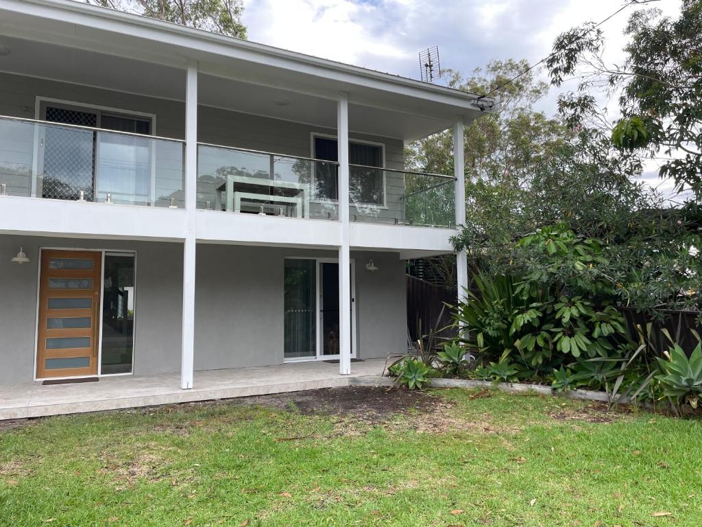 a white house with a balcony and a yard at Coastal Holiday House in Hawks Nest