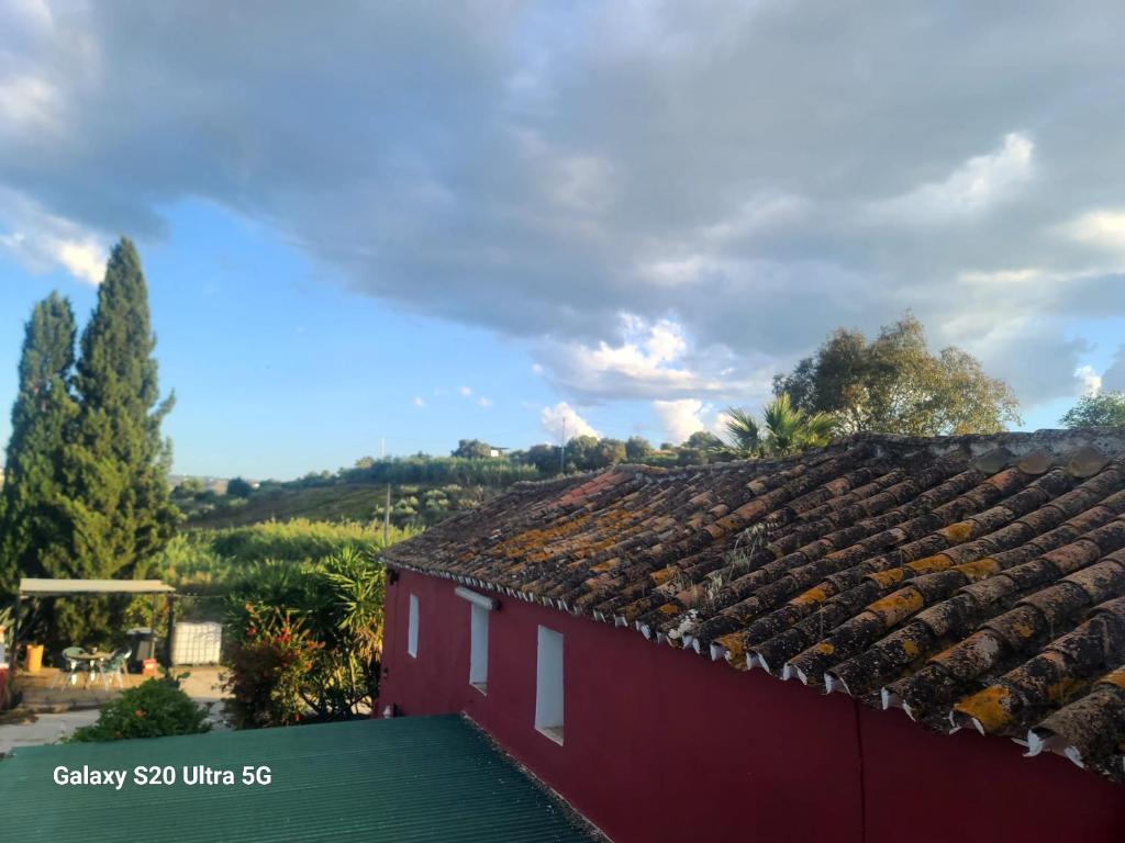 a red building with a tile roof with trees in the background at La Finca Roja una in Málaga
