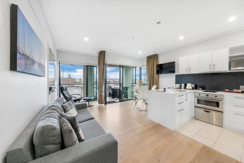 a living room with a couch and a kitchen at Sun Soaked Corner Apartment with Harbour View in Auckland