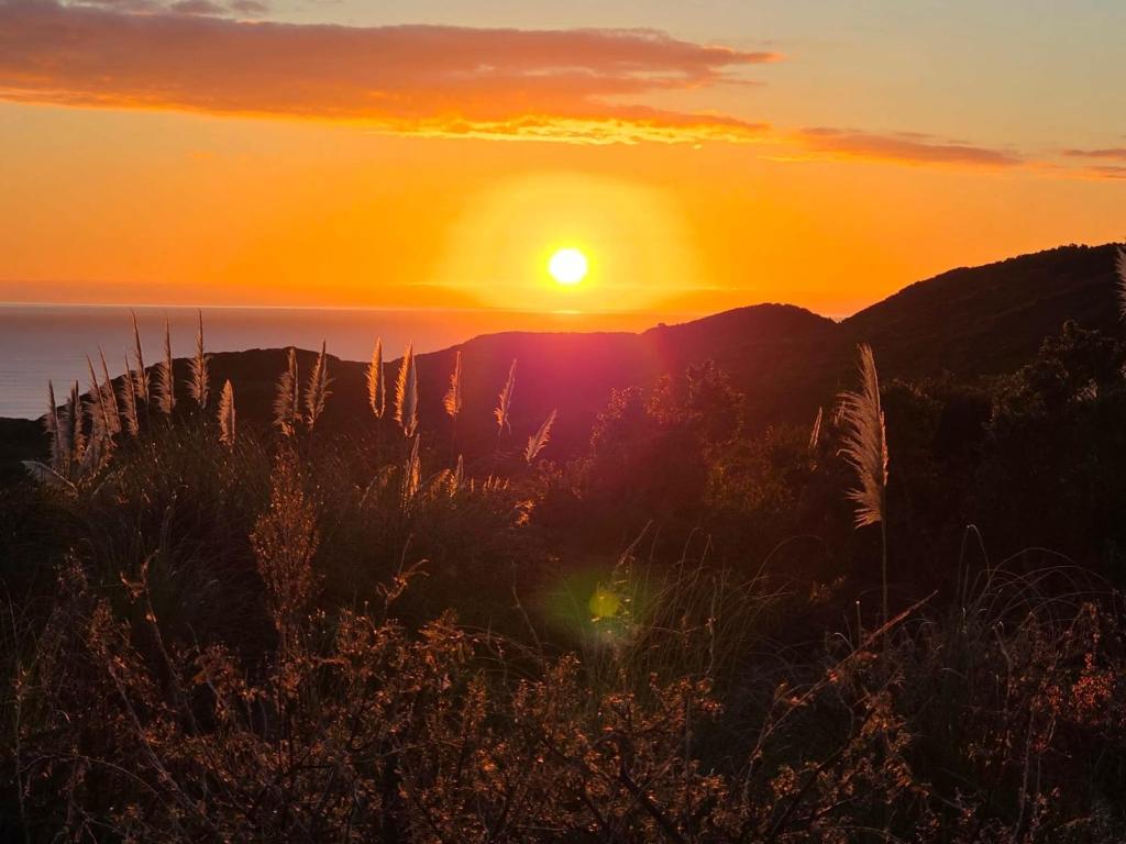 a sunset with the sun setting over the mountains at Rangitoto Retreat Raglan in Te Akau
